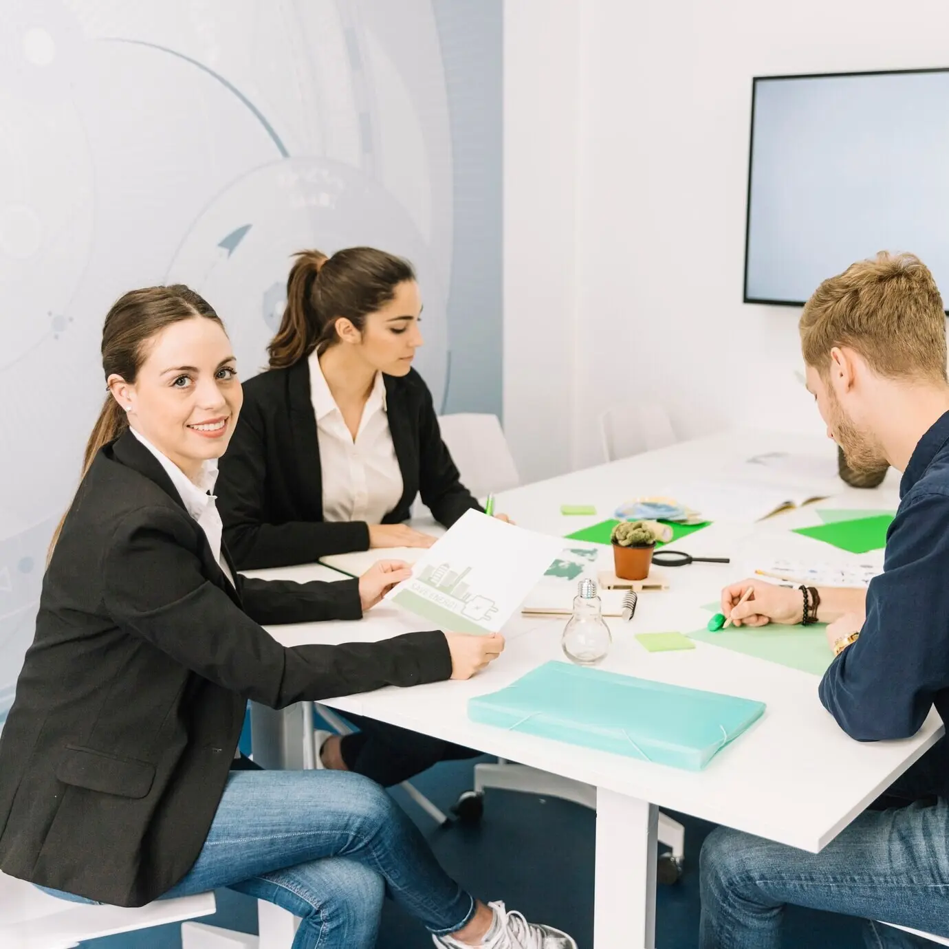 Портрет улыбающейся молодой деловой женщины рядом с ее коллегами, работающими в офисе.